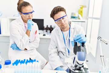 Man and woman wearing scientist uniform looking sample at laboratory