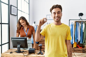 Young hispanic man holding bitcoin virtual money at retail shop looking positive and happy standing and smiling with a confident smile showing teeth