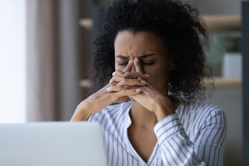 Fototapeta na wymiar Close up unhappy exhausted African American businesswoman feeling pain and dizziness, overworked young female touching nose bridge, suffering from strong headache or migraine after long laptop using