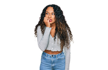 Young hispanic woman with curly hair wearing casual clothes looking stressed and nervous with hands on mouth biting nails. anxiety problem.