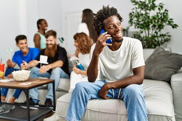 Group of young friends smiling happy sitting on the sofa. Man talking by the smartphone at home.