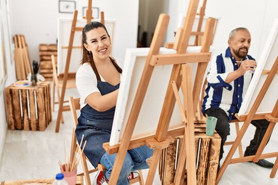 Young artist woman and senior painter man at art studio classroom painting on canvas with brush and oil painting
