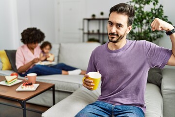 Hispanic father of interracial family drinking a cup coffee strong person showing arm muscle, confident and proud of power