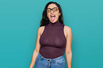 Brunette young woman wearing casual clothes and glasses sticking tongue out happy with funny expression. emotion concept. © Krakenimages.com