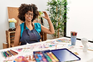 Beautiful african american woman with afro hair painting at art studio smiling and confident gesturing with hand doing small size sign with fingers looking and the camera. measure concept.