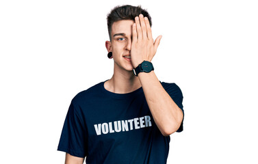 Young caucasian boy with ears dilation wearing volunteer t shirt covering one eye with hand,...