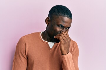 Young african american man wearing casual clothes smelling something stinky and disgusting, intolerable smell, holding breath with fingers on nose. bad smell