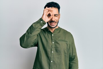 Fototapeta premium Young hispanic man wearing casual clothes doing ok gesture with hand smiling, eye looking through fingers with happy face.