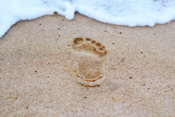 Human footprints in the sand by the sea and sea foam