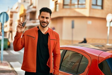 Young hispanic man holding key of new car at the city.