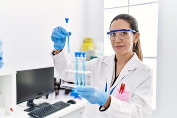 Fototapeta premium Young hispanic woman wearing scientist uniform holding test tube at laboratory
