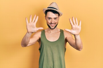 Naklejka premium Young hispanic man wearing summer hat showing and pointing up with fingers number ten while smiling confident and happy.