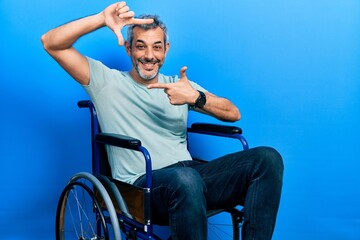 Obraz premium Handsome middle age man with grey hair sitting on wheelchair smiling making frame with hands and fingers with happy face. creativity and photography concept.