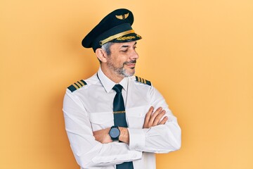 Handsome middle age man with grey hair wearing airplane pilot uniform looking to the side with arms crossed convinced and confident
