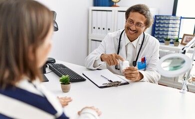 Fototapeta na wymiar Middle age man and woman wearing doctor uniform having medical consultation holding pills at clinic