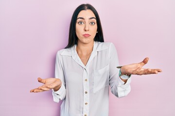 Beautiful woman with blue eyes wearing casual white shirt clueless and confused expression with arms and hands raised. doubt concept.