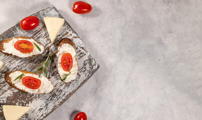 Cream cheese sandwiches with tomato and rosemary on wooden board on grey background, flat lay with free space for text
