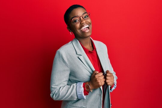 Young african american woman wearing business jacket and glasses winking looking at the camera with sexy expression, cheerful and happy face.