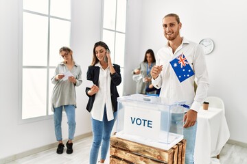 Young australian voter man smiling happy holding australian flag standing by ballot at vote center.