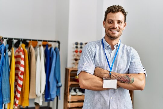 Young hispanic shopkeeper man smiling happy standing with arms crossed gesture at clothing store.