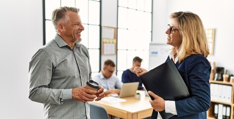 Two middle age business workers speaking while partners working at the office.