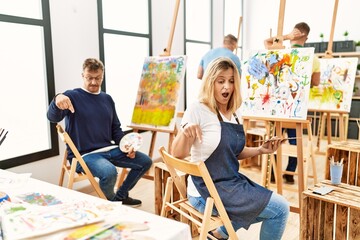 Group of middle age artist at art studio pointing down with fingers showing advertisement, surprised face and open mouth