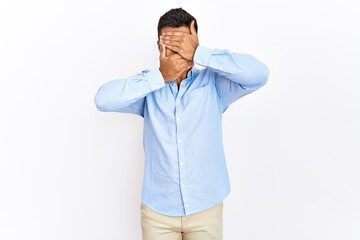 Fototapeta premium Young hispanic man wearing business shirt standing over isolated background covering eyes and mouth with hands, surprised and shocked. hiding emotion