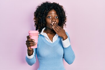 Young african american woman drinking take away coffee covering mouth with hand, shocked and afraid...
