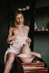 talented sculptor girl in thin light negligee sculpts a jug of clay in pottery workshop near large window. Concept art of sculpture
