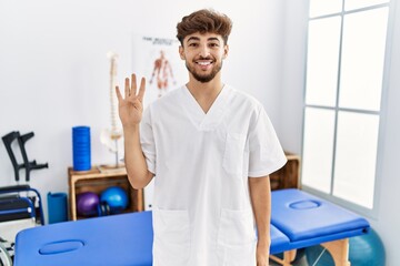 Obraz premium Young arab man working at pain recovery clinic showing and pointing up with fingers number four while smiling confident and happy.