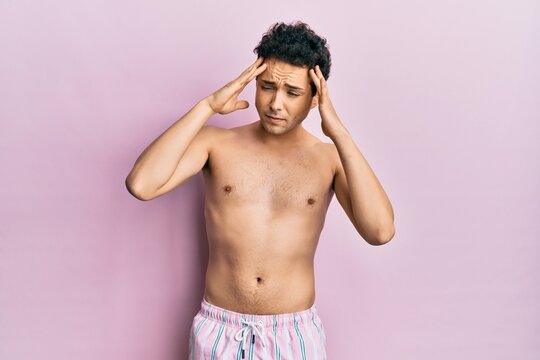 Young handsome man wearing swimwear shirtless with hand on head for pain in head because stress. suffering migraine.