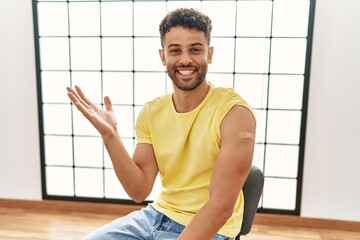 Arab young man getting vaccine showing arm with band aid celebrating victory with happy smile and...