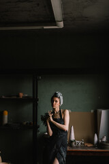 beautiful sculptor girl with bandage on her head and a black apron on her naked body is standing in pottery workshop near large window. concept is beauty and art.