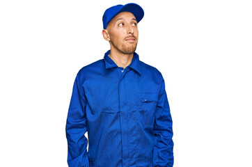 Bald man with beard wearing builder jumpsuit uniform smiling looking to the side and staring away thinking.