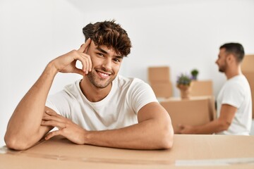 Two hispanic men couple smiling confident leaning on cardboard box at new home