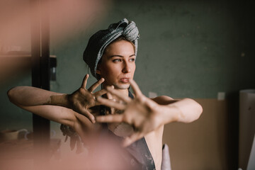 beautiful sculptor girl with a headband and a black apron shows her hands stained with clay. camera focus is on girl's face, blur is on her hands.