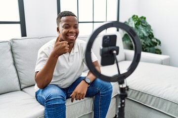 Young african man recording vlog tutorial with smartphone at home smiling happy and positive, thumb up doing excellent and approval sign