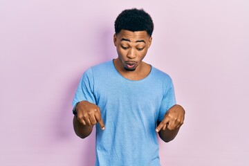 Young african american man wearing casual blue t shirt pointing down with fingers showing advertisement, surprised face and open mouth