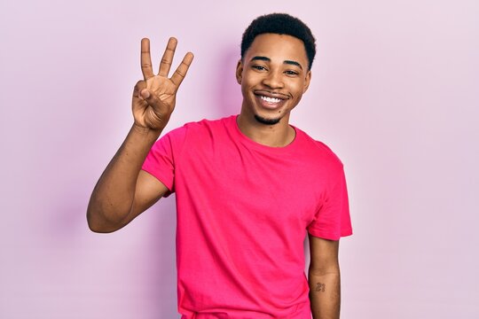 Young african american man wearing casua t shirt showing and pointing up with fingers number three while smiling confident and happy.