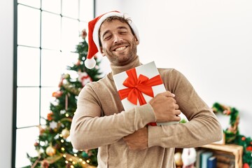 Young hispanic man smiling confident holding christmas gift at home