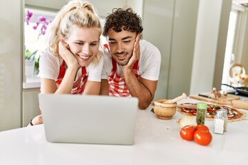 Young couple smiling happy using laptop at kitchen.