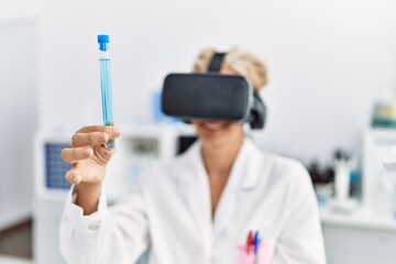 Middle age blonde woman wearing scientist uniform using vr goggles working at laboratory