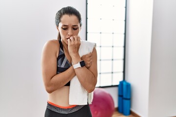 Fototapeta na wymiar Young brunette woman wearing sportswear and towel at the gym looking stressed and nervous with hands on mouth biting nails. anxiety problem.