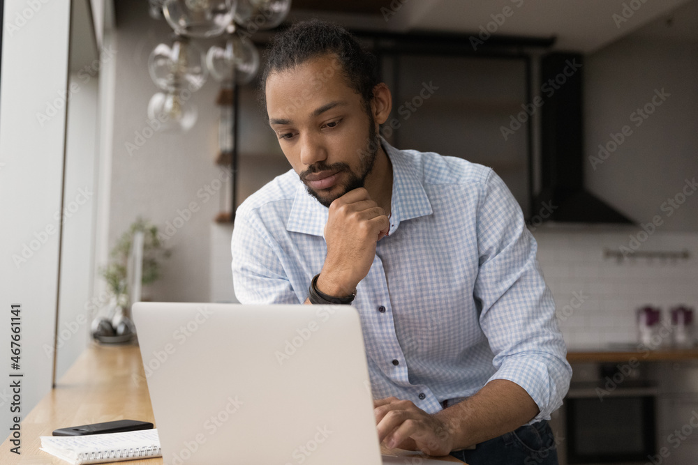 Poster pensive young african american businessman ceo executive manager looking at laptop screen, consideri