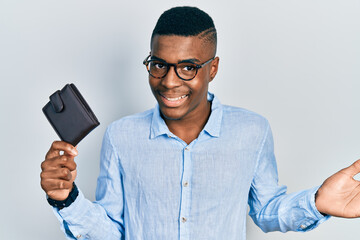 Young african american man wearing glasses holding leather wallet celebrating achievement with happy smile and winner expression with raised hand