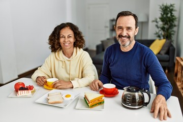 Middle age hispanic couple smiling happy sitting on the table having breakfast at home.
