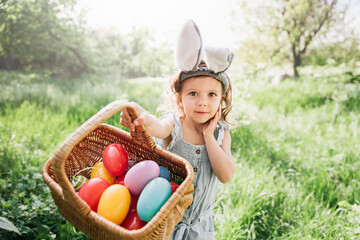 Baby with basket full of colorful eggs. Easter egg hunt. - 467663566