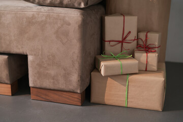 Presents in paper wrap with ribbons under christmas tree indoor near couch with warm light