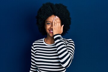 Fototapeta na wymiar Young african american woman wearing casual clothes covering one eye with hand, confident smile on face and surprise emotion.