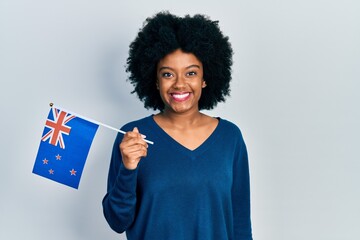Young african american woman holding new zealand flag looking positive and happy standing and smiling with a confident smile showing teeth